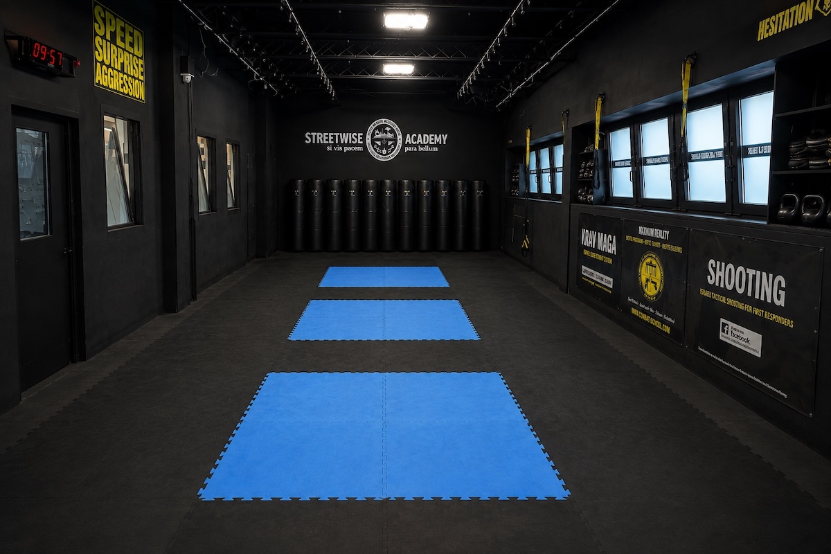 Trainingshalle der Streetwise Academy Berlin mit blauen Matten, Boxsäcken und Logo an der Stirnwand